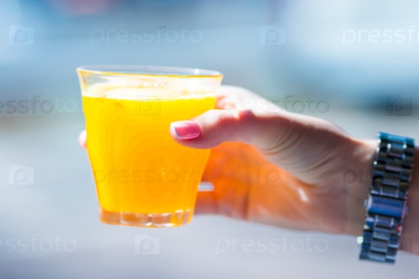 Hand holding glass with fresh orange juice in outdoor cafe, stock photo
