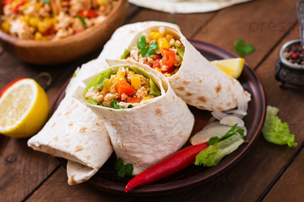 Burritos wraps with chicken meat, corn, tomatoes and peppers on wooden background, stock photo