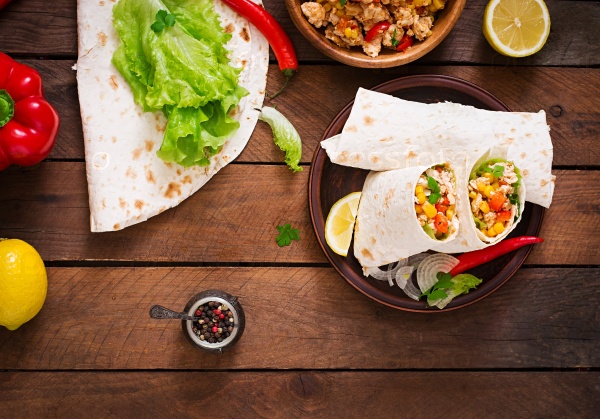 Burritos wraps with chicken meat, corn, tomatoes and peppers on wooden background. Top view, stock photo