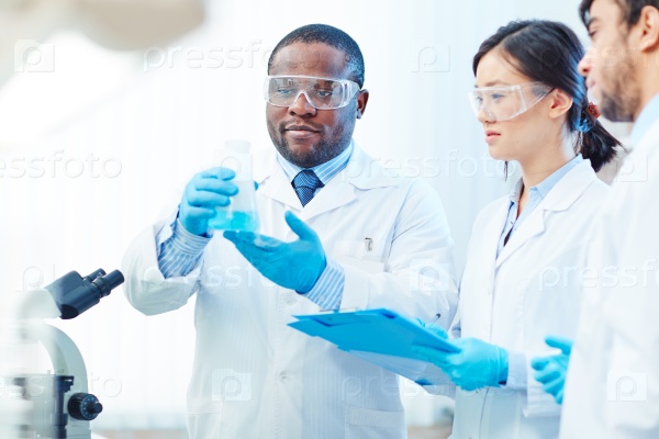 Group of chemists looking at blue liquid substance in tube, stock photo