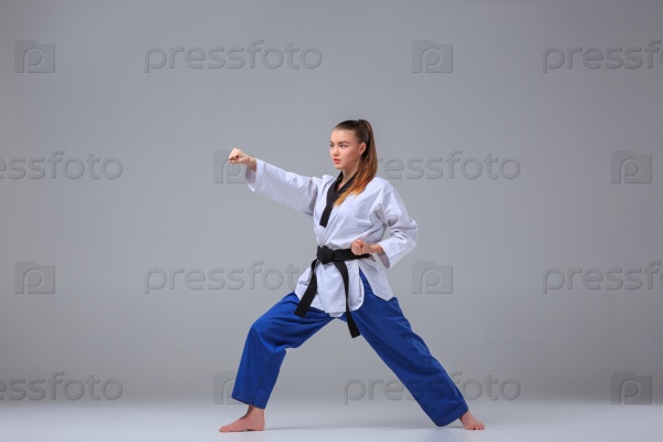 The karate girl in white kimono and black belt training karate over gray background, stock photo