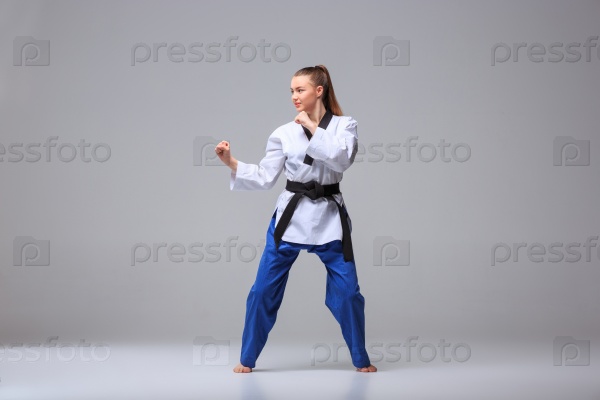 The karate girl in white kimono and black belt training karate over gray background, stock photo