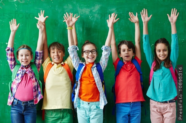 Happy pupils raising hands against blackboard, stock photo