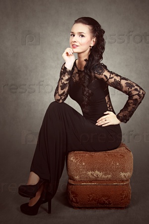 Vintage stylized portrait of a young attractive woman sitting on a padded stool over grey background
