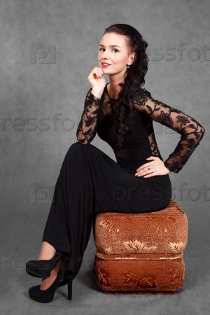 Portrait of a young attractive woman sitting on a padded stool over grey background