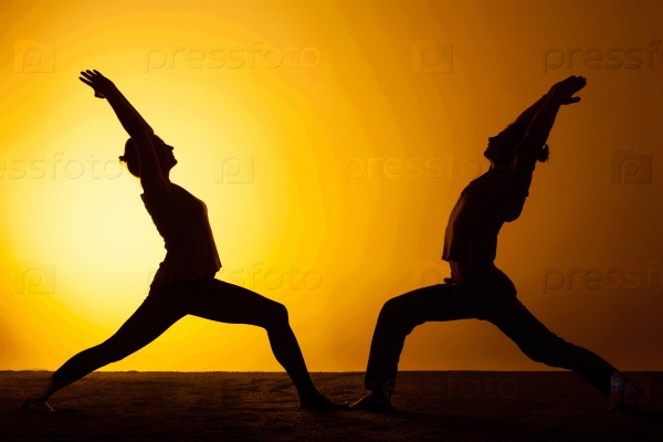 The two silhouettes of people practicing yoga in the sunset light, stock photo