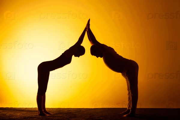 The two silhouettes of people practicing yoga in the sunset light, stock photo