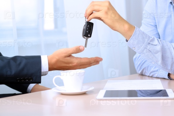 Car salesman handing over the keys for a new car to a young businessman. Focus on a key