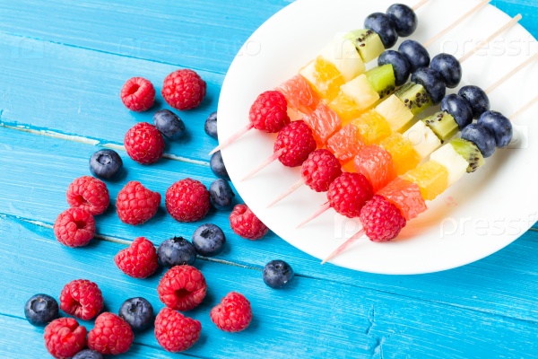 Fresh fruits on skewers in plate on wooden table, stock photo