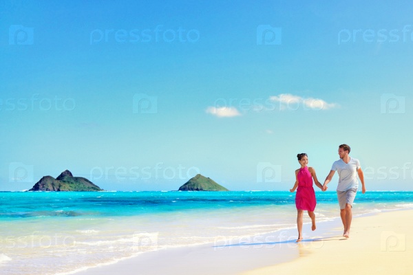 Hawaii vacation couple walking relaxing on white sand and pristine turquoise ocean water on Hawaiian beach Lanikai, Oahu island, USA. Holiday background with blue sky copy-space for travel concept.