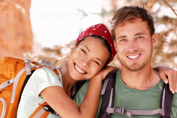 Happy young hikers backpacking on summer travel. Portrait of two friends teenagers or student couple wearing rucksacks bags smiling hiking during road trip vacation or doing volunteering.