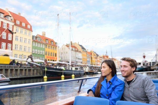 Copenhagen tourists people on cruise boat tour on water canal in old port Nyhavn. Young multiracial couple visiting famous European destination in Europe during fall or spring.