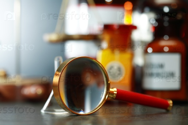 Magnifying glass and chemical funnel against blurred background with old flasks, stock photo