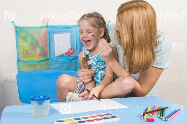 Mother tickles the cheek with a brush to paint his daughter, five-year, stock photo
