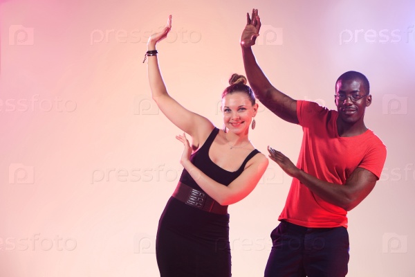 The young cool black man in a red shirt and caucasian woman dancing in studio pink light, stock photo