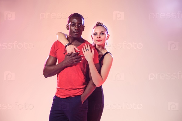 The young cool black man in a red shirt and caucasian woman posing in studio pink light, stock photo