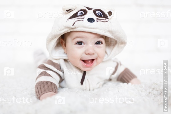 Little boy dressed in raccoon suit and lying on a white soft rug in studio, stock photo