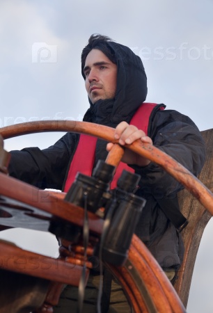 Young sailor on a ship\'s deck behind a steering wheel
