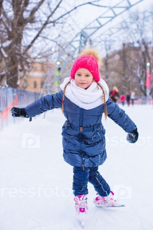 Adorable little girl skating on the ice rink outdoors