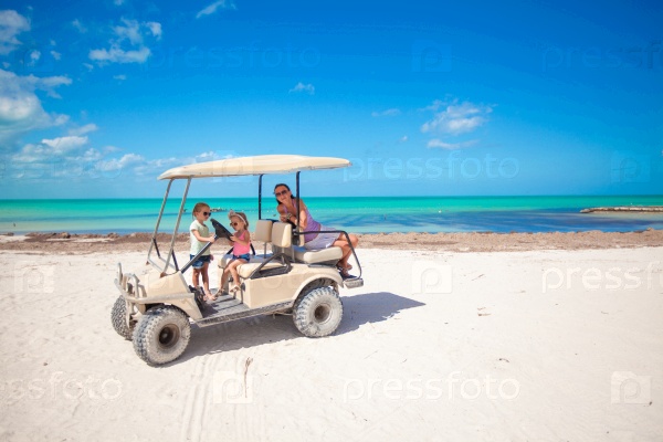 Little girls and their mother driving golf cart at tropical beach, stock photo