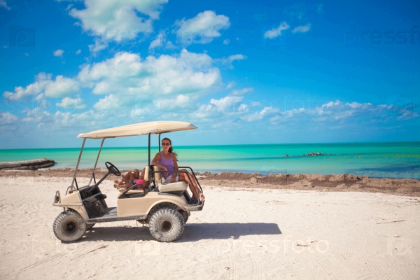 Little girls and their mother driving golf cart at tropical beach