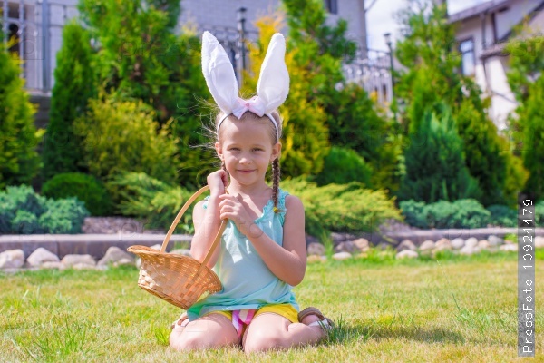 Adorable little girl wearing bunny ears holding basket with Easter eggs