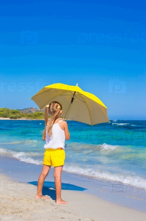 Little adorable girl with big yellow umbrella on tropical beach