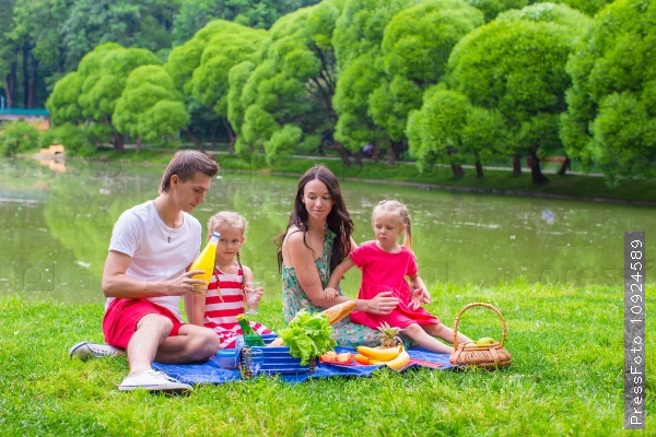 Happy parents and two kids picnicking outdoors