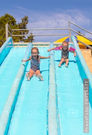 Cute girls on water slide at aquapark during summer holiday