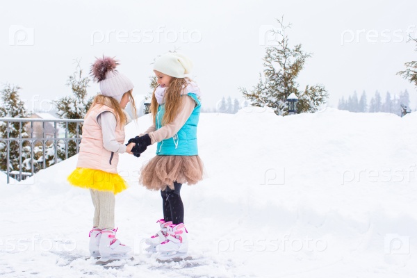 Little girls skating on ice rink outdoors in winter snow day