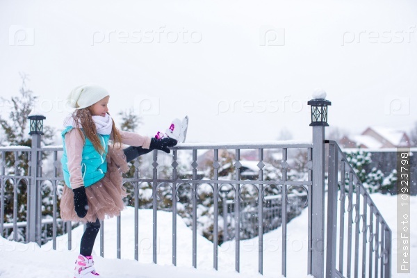 Adorable little girl skating on ice rink outdoors in winter snow day