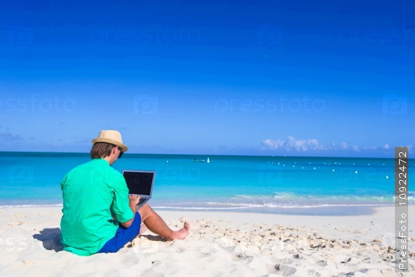 Young man working on laptop at tropical beach, stock photo