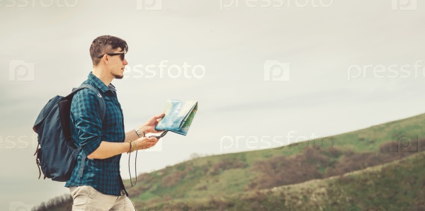 Hiker young man with map and compass searching direction in the mountains in summer outdoor, stock photo