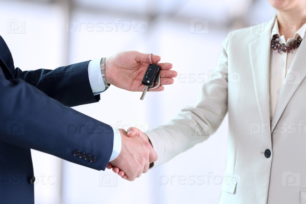 Car saleswoman handing over the keys for a new car to a young businessman . Handshake between two business people