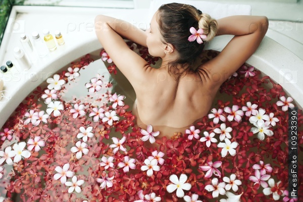 Woman relaxing in round outdoor bath with tropical flowers, organic skin care, luxury spa hotel, lifestyle photo, top view