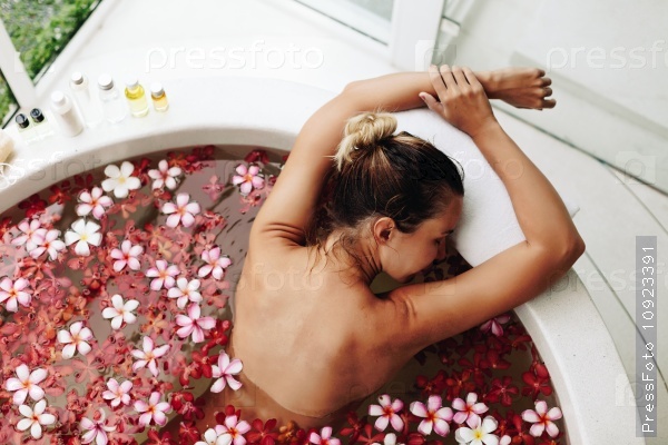 Woman relaxing in round outdoor bath with tropical flowers, organic skin care, luxury spa hotel, lifestyle photo, top view, stock photo
