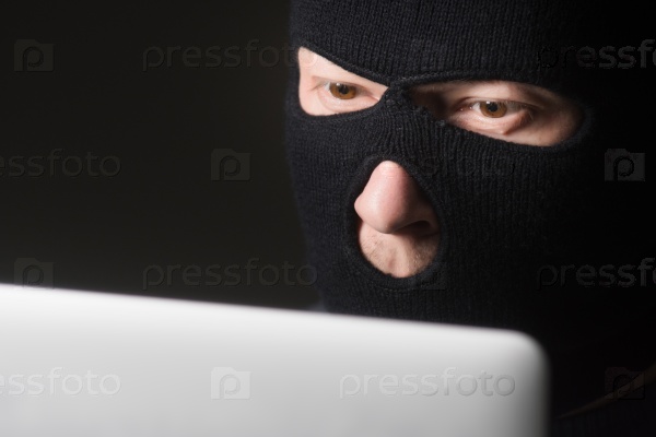 Terrorist in a mask using computer for crime, stock photo
