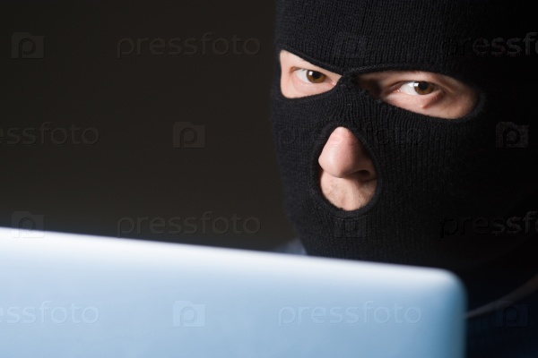 Terrorist in a mask using computer for crime, stock photo
