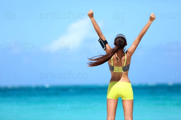 Success fitness woman concept with sports armband and earphones. Winning concept of female athlete runner cheering with arms raised up for achievement in weight loss or life goal.
