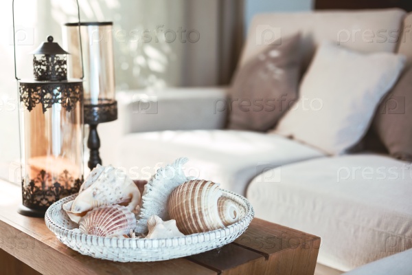 Beach interior decor: sea shells and lanterns on the wooden coffee table, natural colors. Detail of living room.