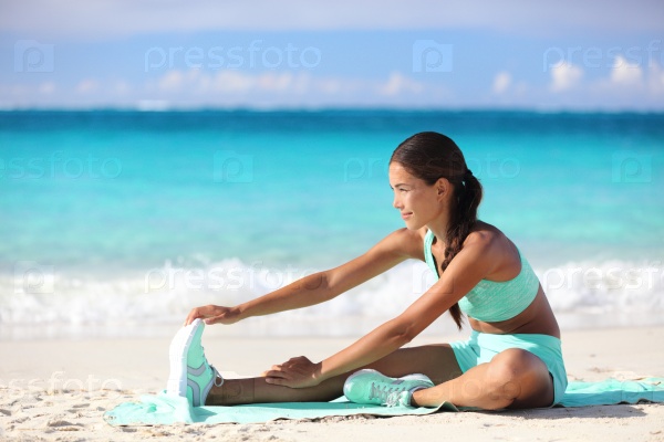 Fitness woman stretching legs on beach - Sporty Asian girl doing leg stretches, sitting one-legged hamstring stretch.  Happy young adult training her body on sunny summer tropical travel beach.