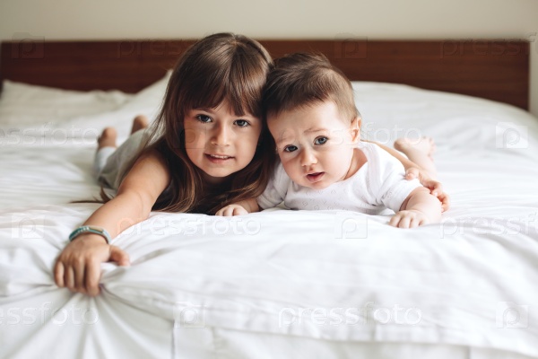 Siblings hugging and laying down on the bed in bedroom, stock photo