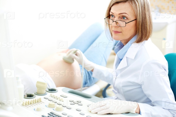 Female doctor doing ultrasound on belly of pregnant woman in clinic, stock photo