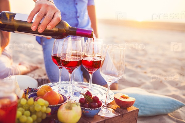 Group of happy friends having red wine on the beach. Sunset beach party