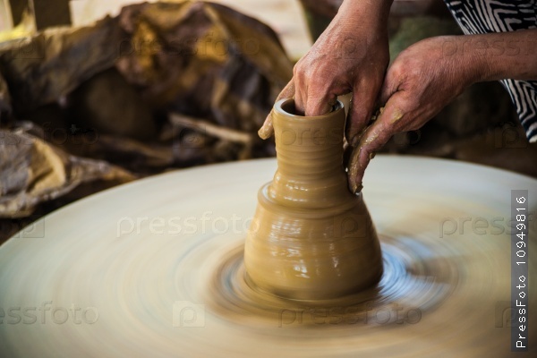Closeup view of hands of a senior asian potter forming clay into a pot on a turntable. Image of asian handcrafts and manuafacture.