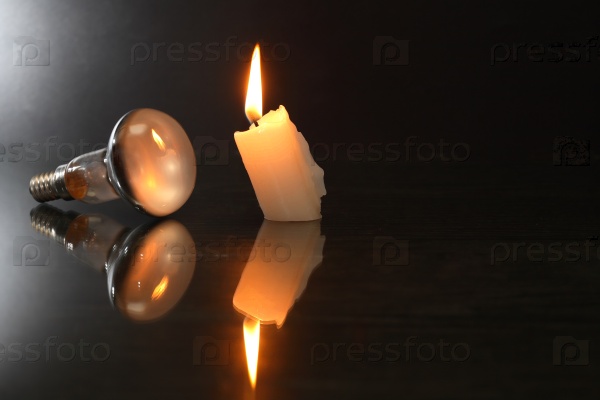 Blackout concept. One electric bulb against candle on dark background