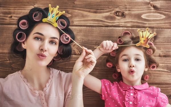 Funny family! Mother and her child daughter girl with a paper accessories. Beauty funny girl holding paper crown on stick. Beautiful young woman holding paper crown on stick.
