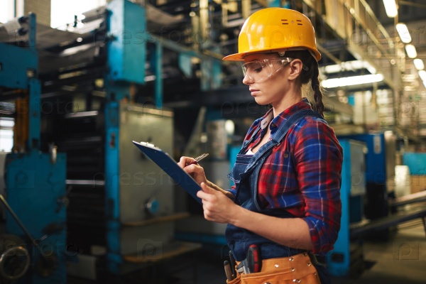 Young woman making notes in document in factory, stock photo