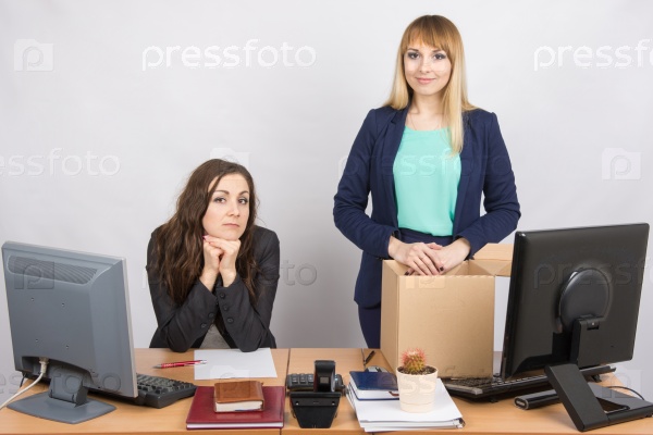The girl in the office is facing the box with things near the colleague sitting next, stock photo