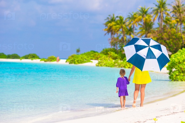 Mother and little girl with umbrella hiding from sun at beach